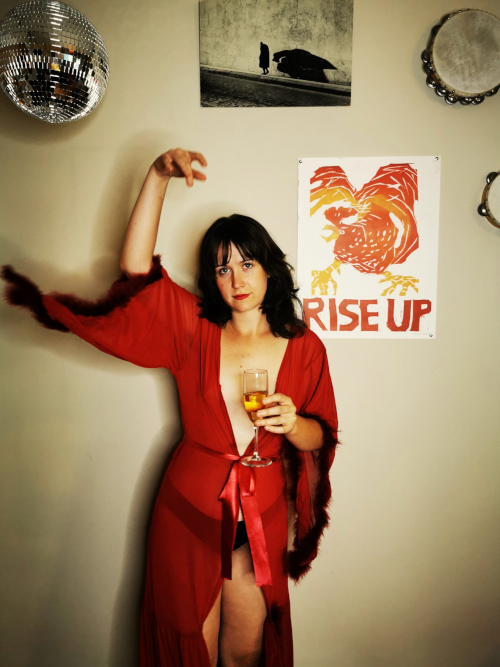A light-skinned artist in a fluffy robe holds a glass of champagne