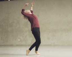 January, 2025. Lisa Kraus dances solo at Tictac Art Centre. Facing stage left, Kraus crosses her left thigh behind her right. Her knees meet. The tops of her left toes press into the ground as her right heel lifts in a demi releve. Kraus releases her sternum to the sky, elbows pulled back, forearms lifted, face tipped toward the ceiling.