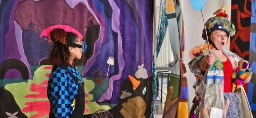 Two people stand in front of a curtain backdrop that’s painted like a trashed cave and swamp. One person is wearing a blue checkered longsleeve shirt with black overalls and big blue swimming goggles, holding the lid to a trash can. Another person is holding a blue fly-swatter in one hand and a toy stuffy in the other. They wear a costume made of trash and repurposed fabrics, and are standing in front of a large plastic trash bag.