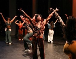 The image features dancers from The UMAMI Colletive’s Sweetest Encounter, wearing various colorful 70s vibe clothing. The ensemble poses with all hands up to the sky and flares outward while they look up. It is set against a warm sunrise background, the dancers radiant happiness through their inviting smiles and open chest to the sky as if soaking in the sun.