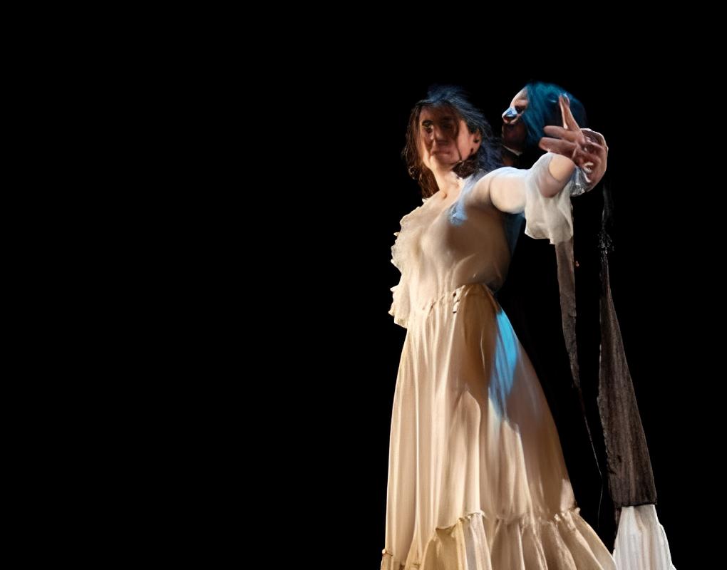 Two bodies pressed almost into each other, fingertips grazing another’s hand. In front, a dancer in a modest white shirt and long skirt glances behind her through tousled hair. A second dancer dressed in black sackcloth hovers behind her, as if readying to whisper something in her ear.