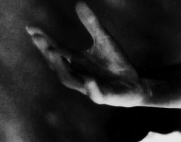 In greyscale photograph, a hand emerges from the dark, fingers shades of white and grey like brushstrokes.