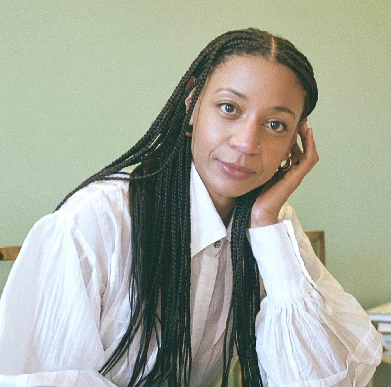 Lauren Morrow, author of Little Movements, stares directly into the camera. She wears a white button-down, and her hair is in long black braids.