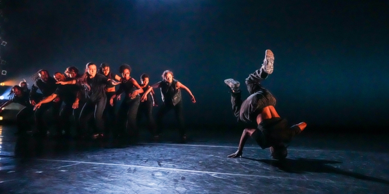 A dancer caught mid-head spin with white sneakers punching into the air while a crowd of others watch intently, arms reaching towards each other.
