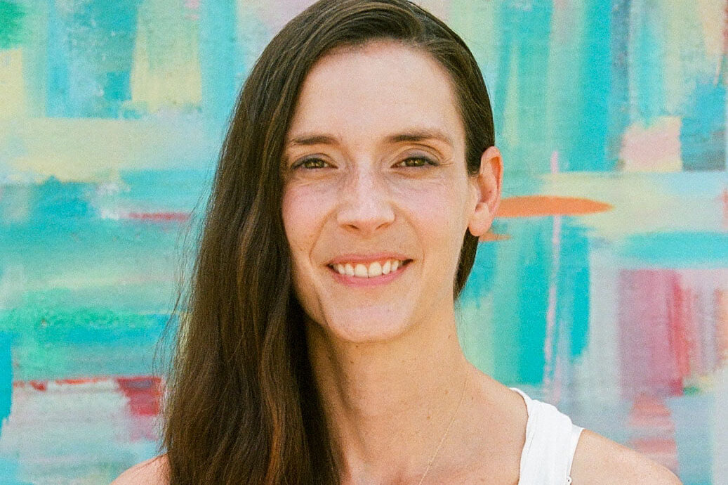 Nicole Perry, the author of "Care-full Creativity in Theatre and Dance Education," smiles directly into the camera. She has wavy brown hair and wears a sleeveless white top.