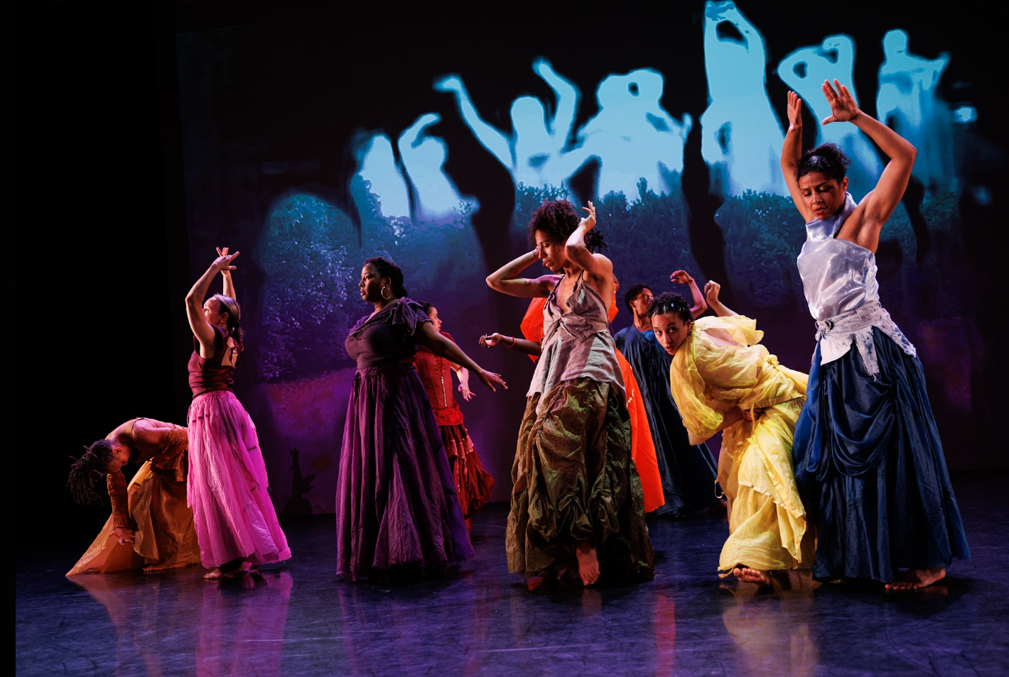 Dancers scattered in a loose line, bend, raise their hands, reach, fold, and step. behind them there is a projected silhouette of this line - a live video feed.