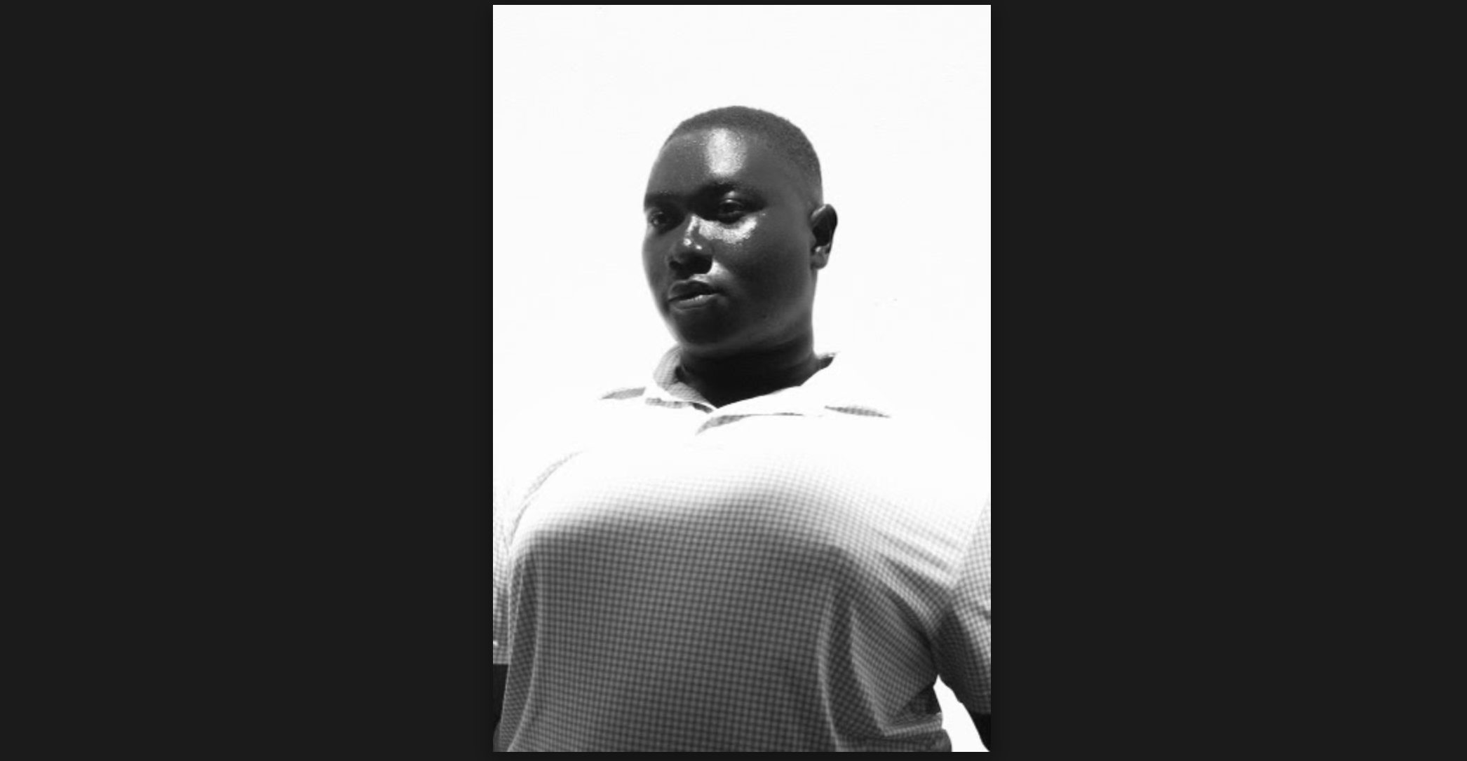 A black and white bust shot of Bempa looking forwards with a serene and powerful expression. He is black and wears his hair short cut in a fade. His chest juts out forwards proudly in his collared cross hatched shirt.