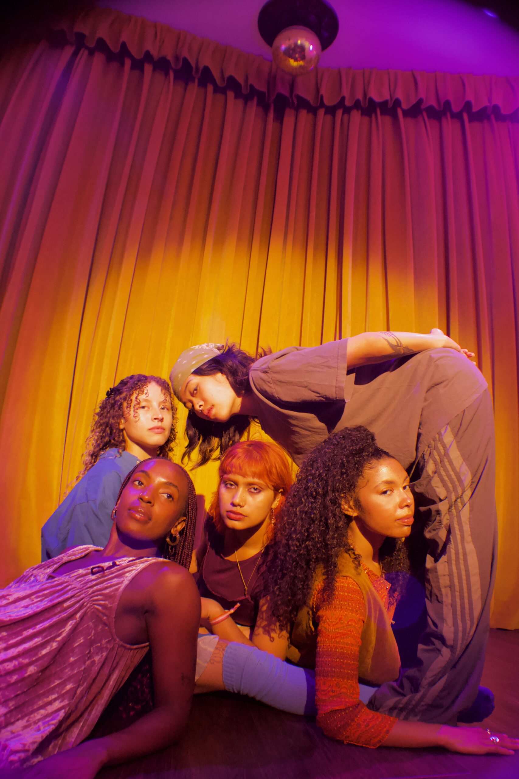 Five dancers look directly or almost into the camera. They’re slightly turned at different angles in different loose-fitting, comfortable clothes.