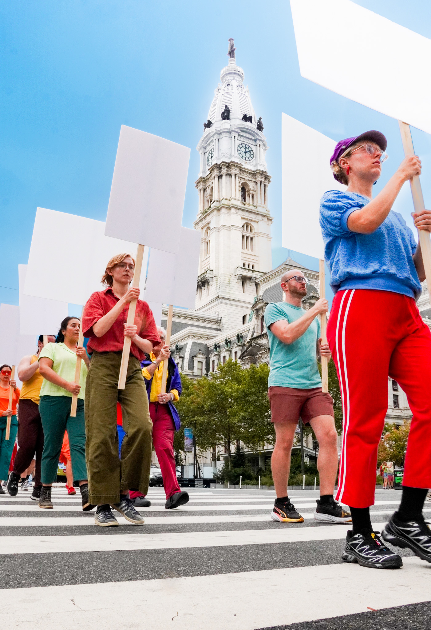 a line of people in brightly colored clothing walk past a court house in Philadelphia carrying blank white signs
