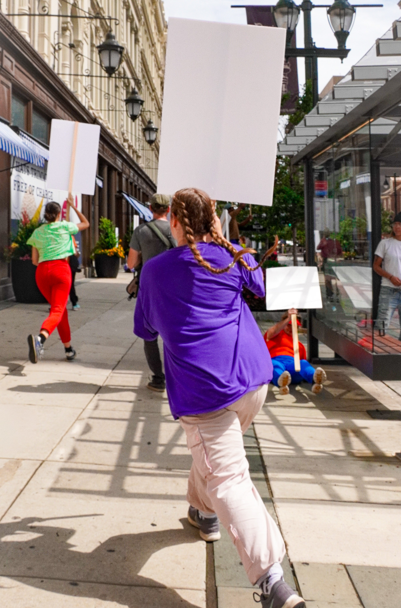 people in brightly colored clothing run down an urban street carrying blank white signs