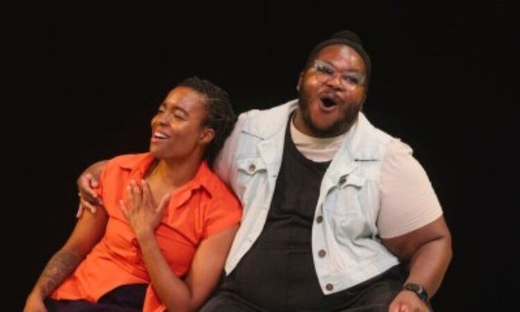 Nicole Y. McClam, a Black woman, leans on Azure D. Osborne-Lee, a disabled Black trans and queer person, as they sit and sing out joyfully. Azure has their arm around Nicole’s shoulders, as Nicole rests a hand on her chest. Photo by Ahad Subzwari/The Shed.