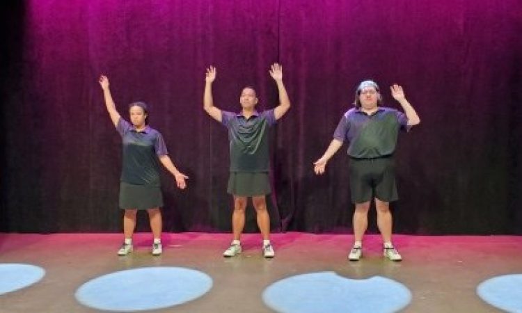 pink backlight, three dancers, left most has right arm up and left arm down, middle has both arms bent upward, right has bent left arm and straight right arm, all in purple polos, two white set pieces frame the image with black curved lines.