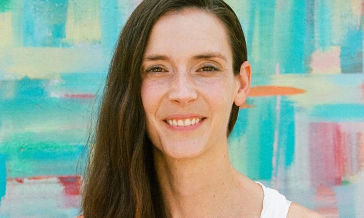 Nicole Perry, the author of "Care-full Creativity in Theatre and Dance Education," smiles directly into the camera. She has wavy brown hair and wears a sleeveless white top.