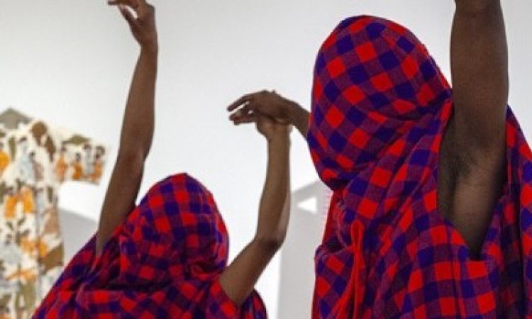 Two figures entwine in a tender embrace, their bodies wrapped in rich layers of Maasai Shuka, hands poised with balletic grace—an intimate tableau of support, connection, and quiet strength.