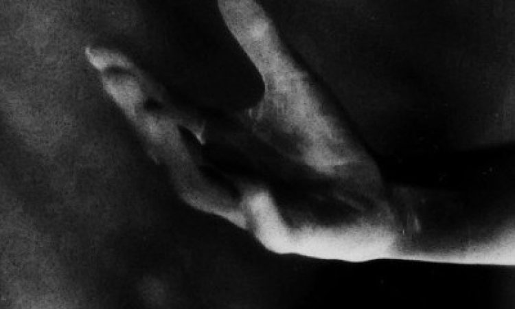 In greyscale photograph, a hand emerges from the dark, fingers shades of white and grey like brushstrokes.