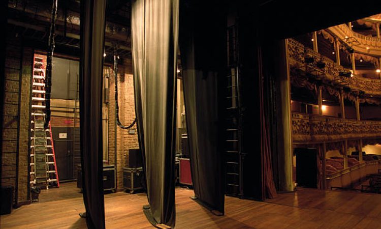 From the stage looking off stage left between the curatins to an empty space, with ladders, lights, and a door.