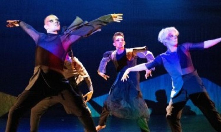 The four dancers of soapbox, each with dark Gothic eye and red facial makeup in tight black pants and tops of geometric blocks of dark blue and black colors stand in a spotlight surrounded by lighting in black, blues and some red hues. Tyler Rivera and Megan Mazarick stare either fearfully or menacingly to the far right in wide stances and extended arms. Behind them, Alonzo Magsino, and, partially hidden, Danielle Currica stare intently in the same direction but with arms folded inward.