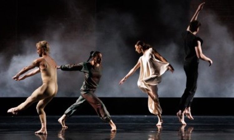 (Left to Right): Spencer Weidie, Jennifer Payan, Ashley Merker, Patrick Needham. Four young dancers are captured in multiple states of joyous abandon. One faces away from us in a tan body-suit that clings to his flesh, his arms and one leg pointing to the corner, while another wearing dark burgundy lunges forward on one leg with her arms extended behind her. A third dancer, wearing white, points to the floor as she tips her long spine to the side; while the fourth, wearing black and with his back to us, has just leapt from the floor, his left arm gently reaching above him.